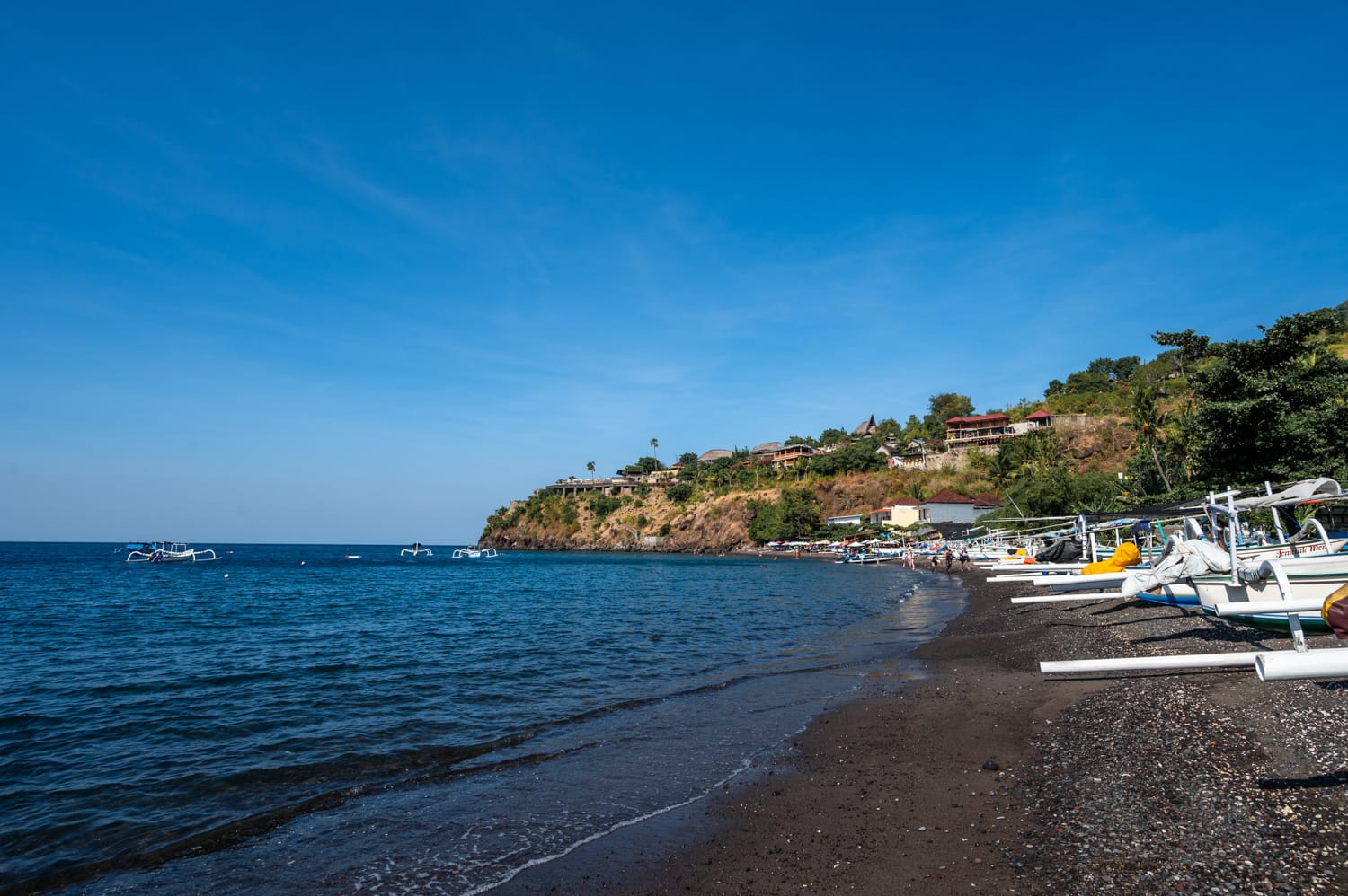 Schwarze Kiesel und Boote am Jemeluk Beach in Amed auf Bali
