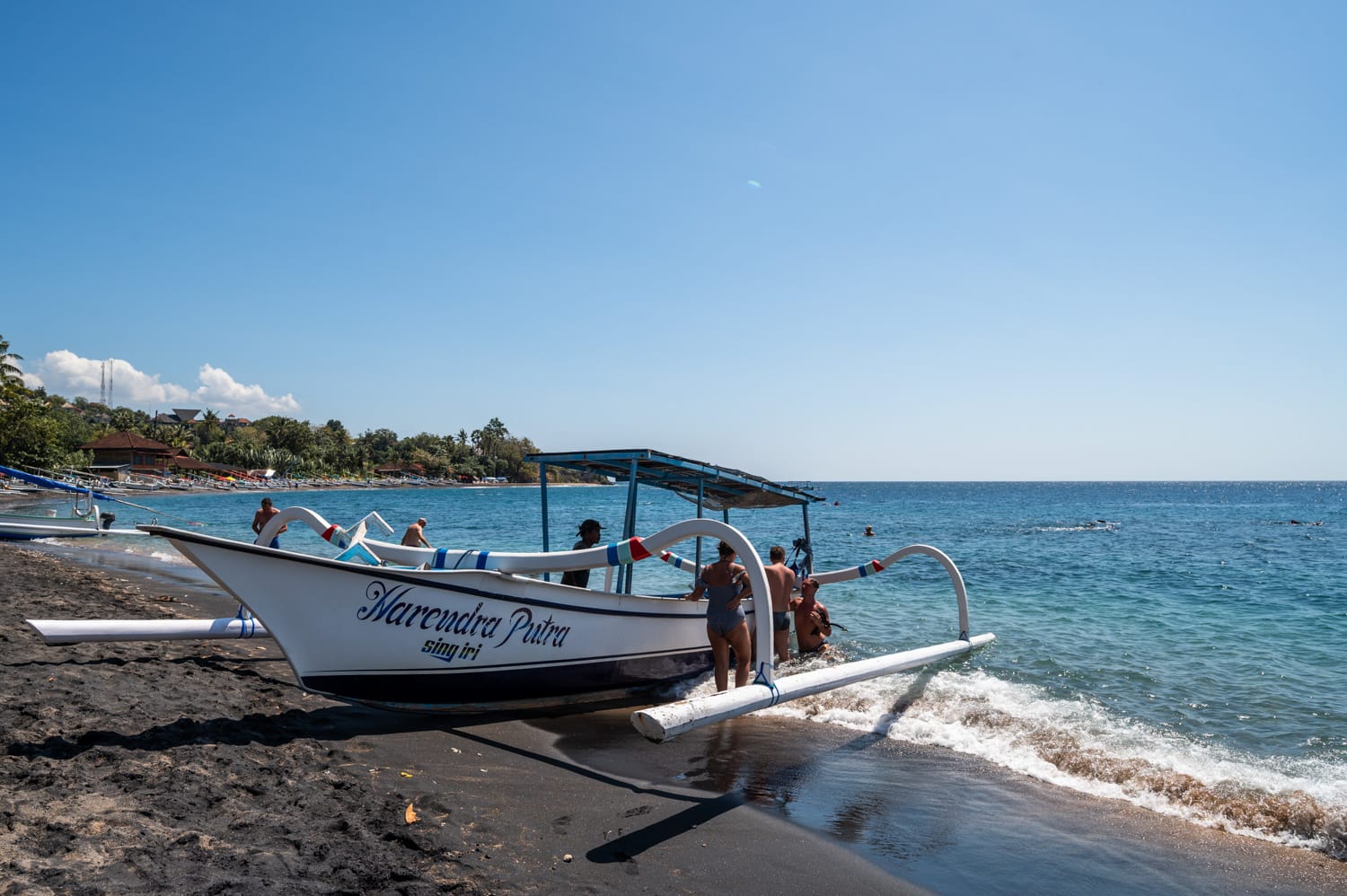 Touristen steigen direkt am Strand in ein Boot für eine Schnorcheltour in Amed auf Bali