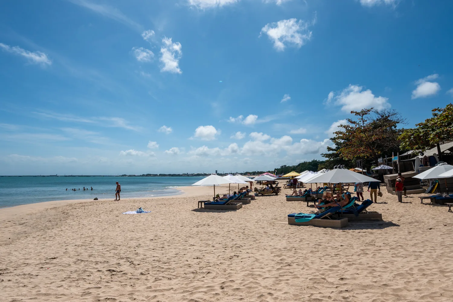 Urlauber baden im flachen Wasser des Jimbaran Beach
