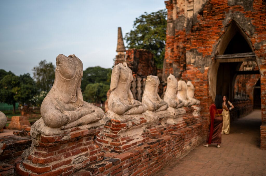 buddhas mit abgeschlagenen köpfen im Wat Chai Watthanaram und frauen in traditionellen thai outfits