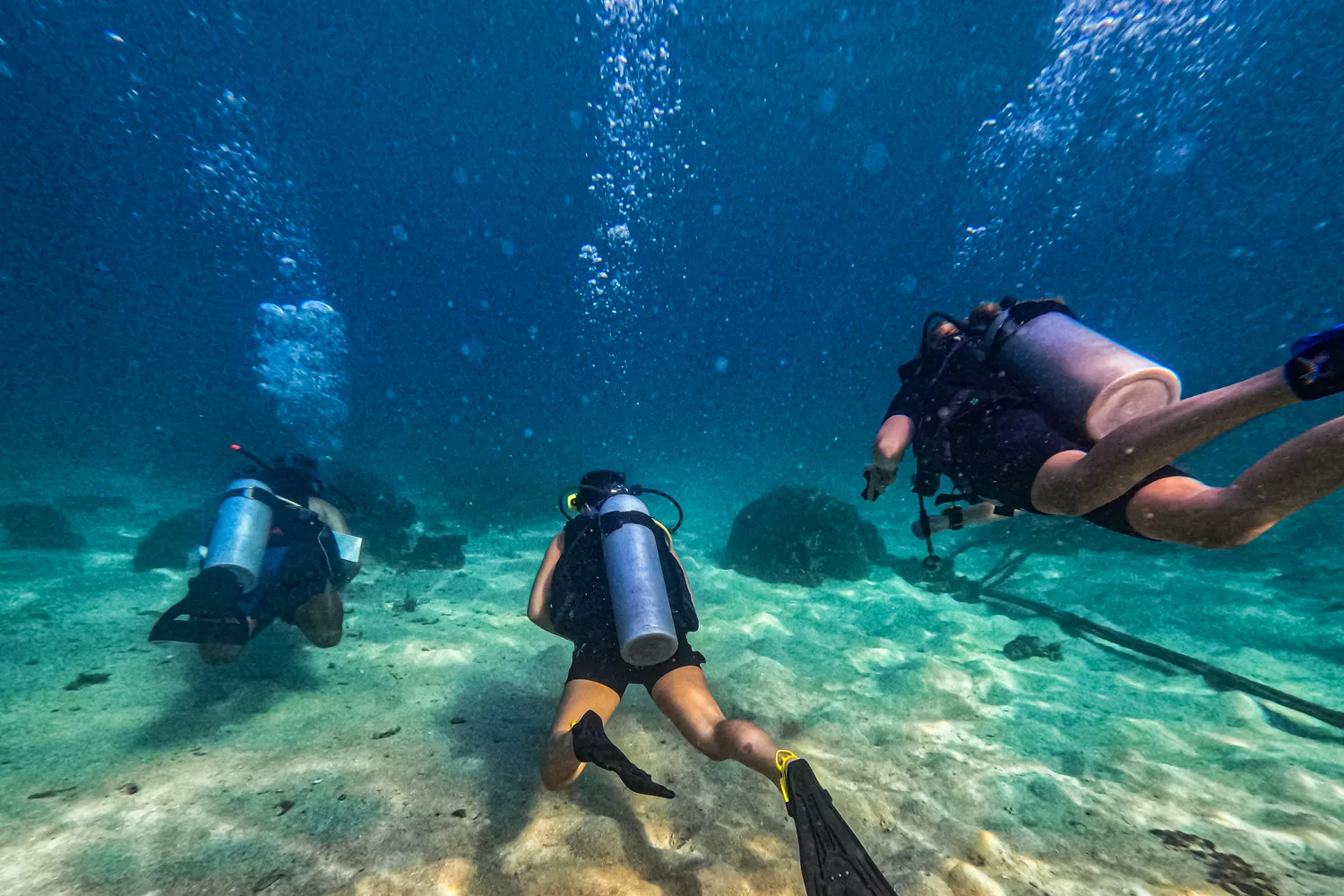 Drei Taucher tauchen vor uns während eines Tauchkurses auf Koh Tao