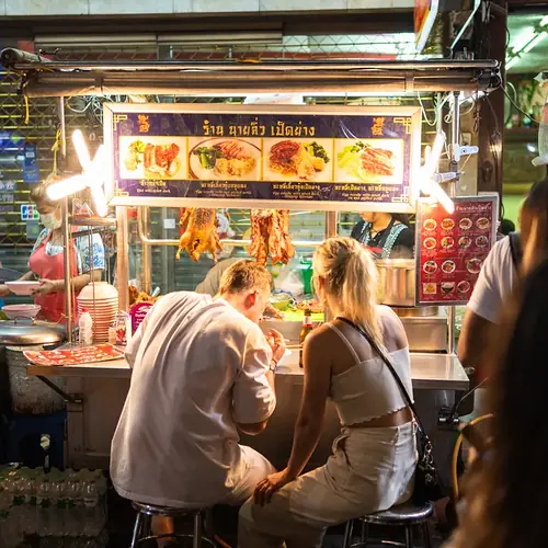 Gäste an einer Garküche am Abend in Chinatown in Bangkok