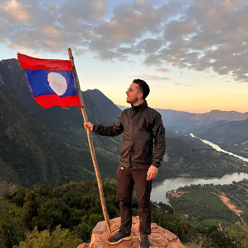 Alex mit der Flagge von Laos auf einem Gipfel über Nong Khiaw und dem Fluss Nam Ou