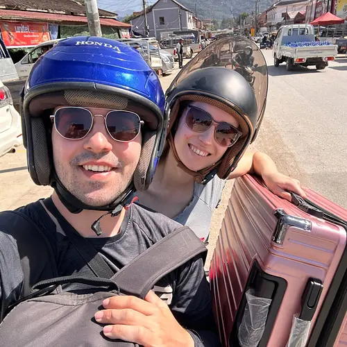 Vanessa und Alex mit Helmen auf dem Roller in Luang Prabang, dazu ein rosa Koffer